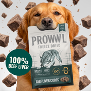 A golden retriever dog holds a bag of Prowvl Freeze Dried Beef Liver Cubes. The bag is white and dark green with an illustration of a wolf.